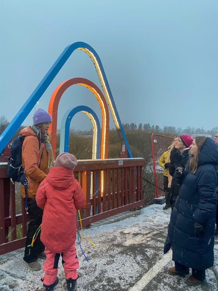 Folk står ved farverig lysinstallation på bro i vintervejr