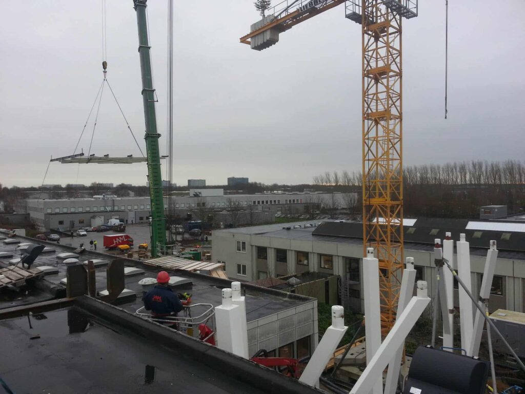 Byggeplads med kraner og arbejdstagere løfter stålplade