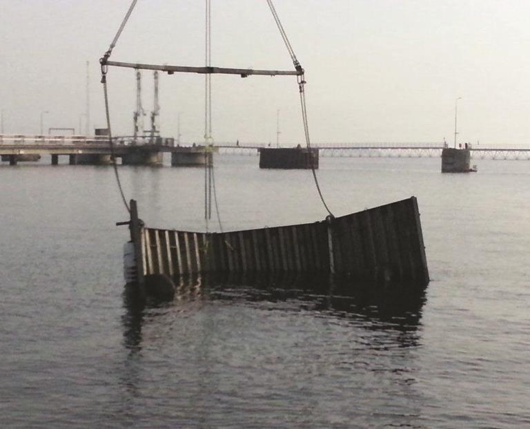 Nedsænket metalstruktur hæves fra vand nær havn