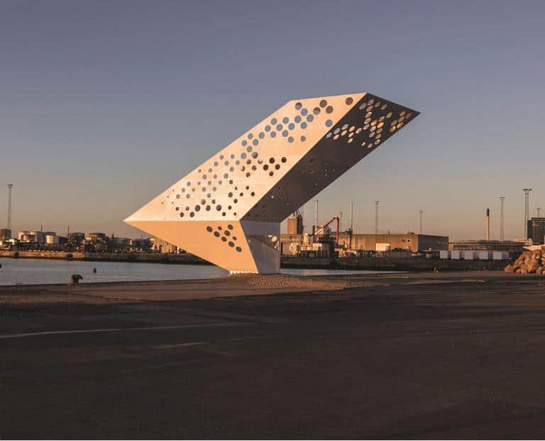 Moderne hvid skulptur ved havneområde i solnedgang