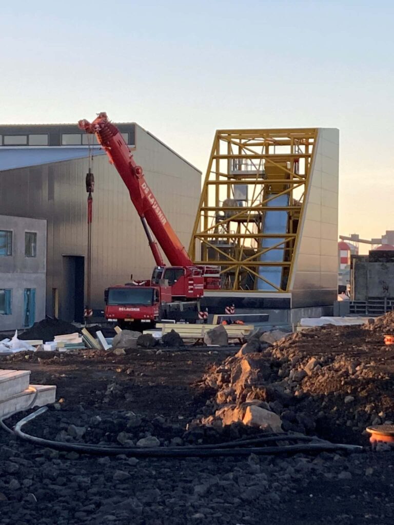 Rød kran løfter stålkonstruktion på byggeplads